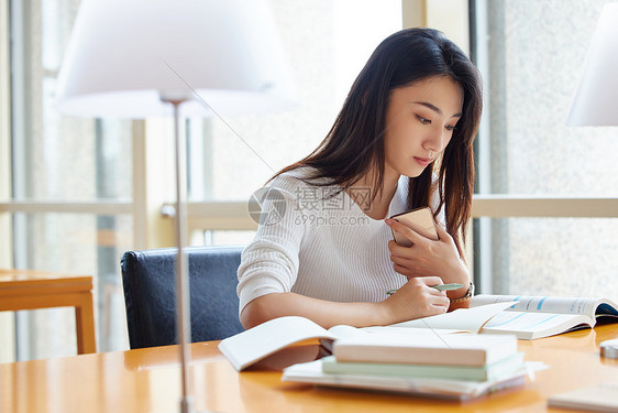 女学生图书馆学习使用手机查资料图片