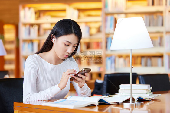 女学生图书馆学习使用手机查资料图片