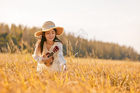 成熟水稻手拿尤克里里走在稻田的年轻女性背景