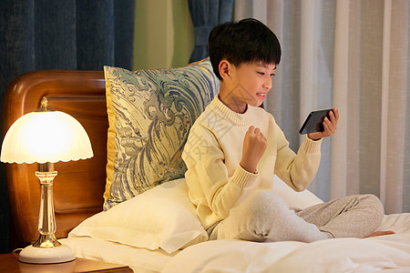 小男孩睡前躺在床上玩手机图片