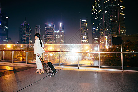 都市女性夜晚拉着行李箱在天桥上图片