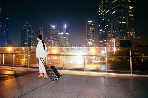 都市女性夜晚拉着行李箱在天桥上图片