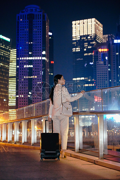 都市女性夜晚手拉行李箱走在天桥上图片