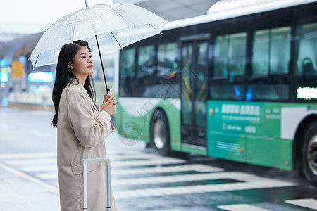 整理行李箱在机场室外撑伞等车的女性背景