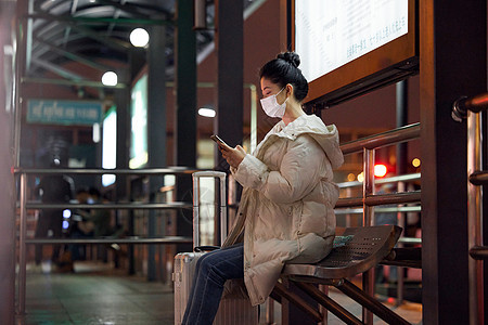 戴口罩的美女夜间出行坐在站台等待公交车图片