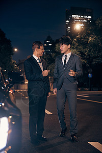夜晚站在车边讨论工作的商务男性形象图片