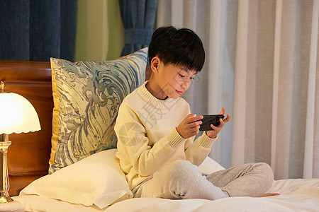 人在卧室小男孩睡前躺在床上玩手机背景