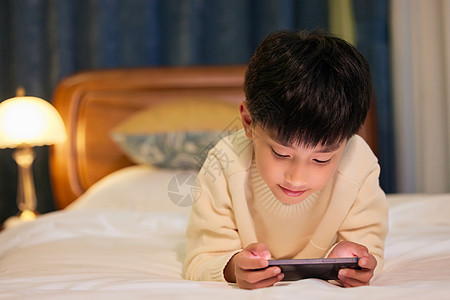 小男孩睡前躺在床上玩手机图片