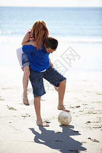 男孩背着女孩在海滩上看足球图片