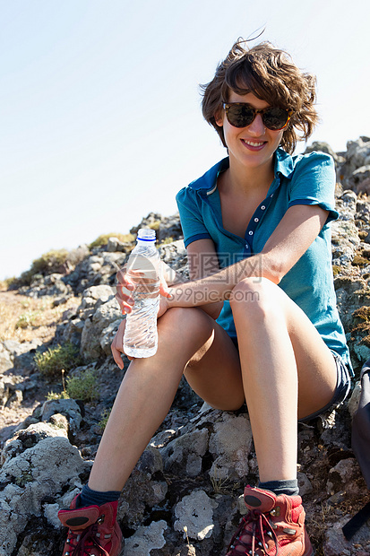 坐在岩石上喝水的女性图片