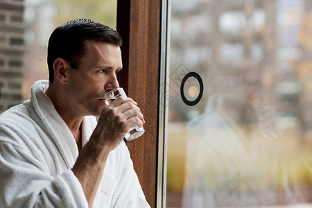 男人穿着浴袍喝水望向窗外图片