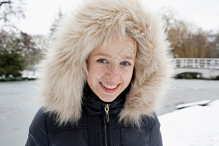在雪中穿着毛皮兜帽的微笑女孩图片