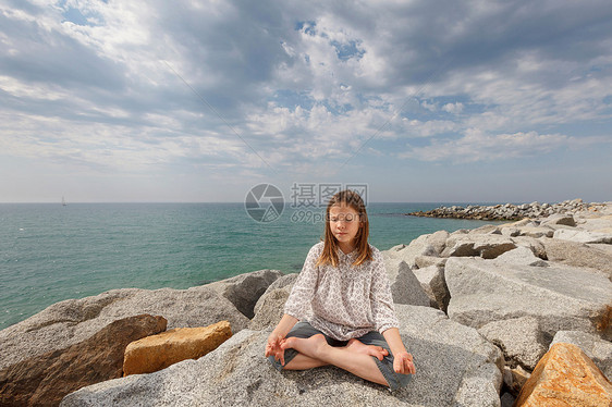 女孩在海滩的岩石上冥想图片