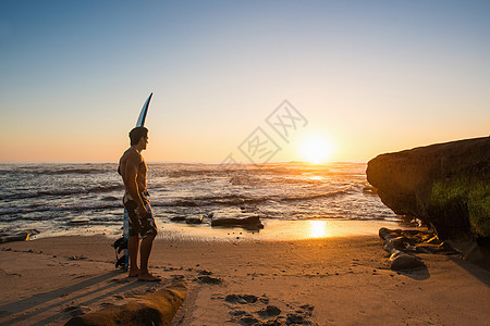 男子在岩石海滩上携带冲浪板图片