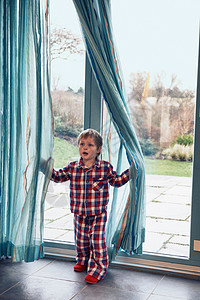 穿着睡衣的男孩在窗帘里玩图片