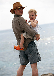 抱着婴儿的父亲父亲抱着儿子站在海边背景