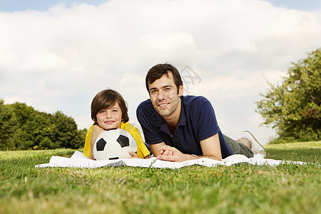 父亲和抱着橄榄球的儿子躺在毯子上图片