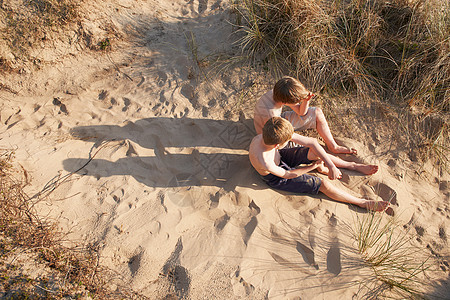 两个男孩坐在沙滩上图片