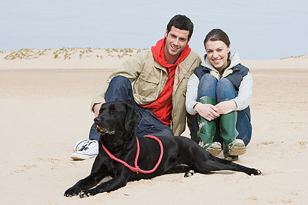 夫妻与宠物狗坐在沙滩上图片