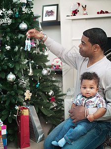父亲和婴儿男孩装饰圣诞树图片