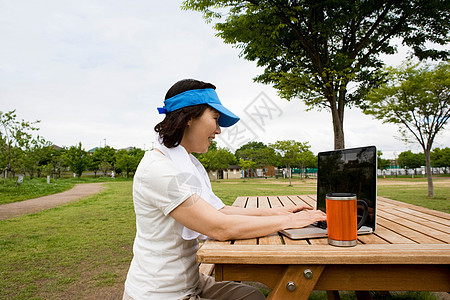 妇女在公园野餐席上使用笔记本电脑图片