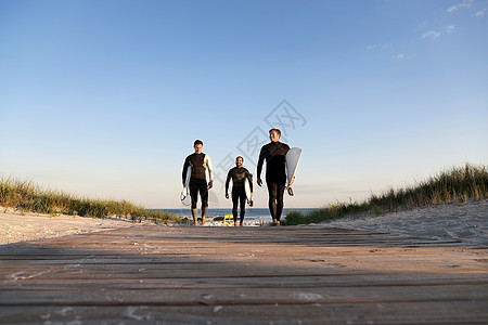 三名冲浪者走在人行道上图片