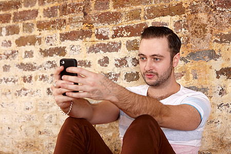 男人靠在砖墙上玩手机图片