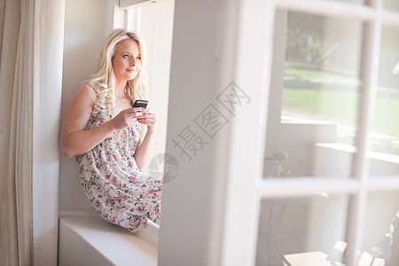 坐在窗台上拿着智能手机的年轻女子图片