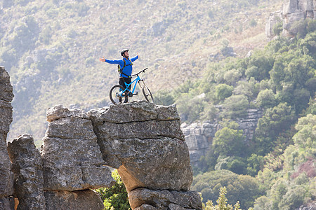骑着山地车在岩石上伸展的青年男子图片