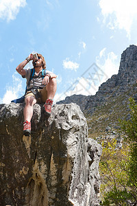 坐在岩层上喝水休息的男徒步者图片