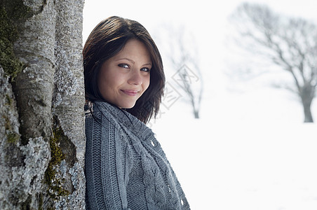 年轻女在雪地上靠着树木图片