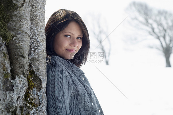 年轻女在雪地上靠着树木图片