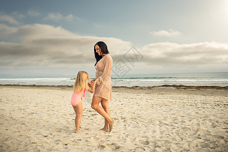 在海滩上与女儿牵手的年轻女子图片