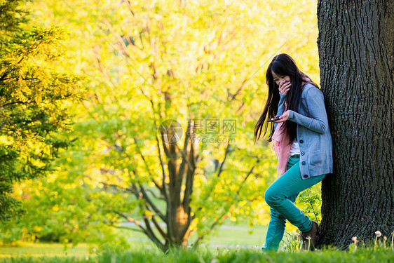 年轻女孩在公园里看着手机捂嘴偷笑图片