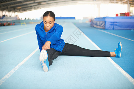 坐在地板触摸脚趾的年轻女运动员图片