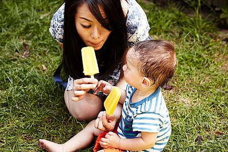 母亲和儿子坐在草地上吃冰棒图片