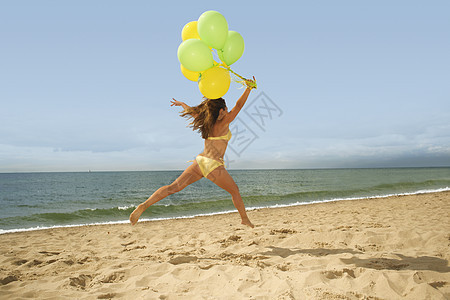 女人在海滩上拿着气球跳起来图片