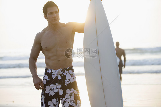拿着冲浪板站在海滩上的男人图片