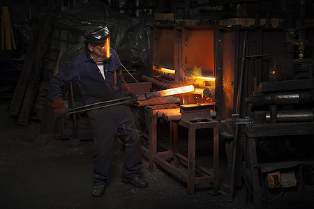 工厂内工人夹起烧红的铁块图片