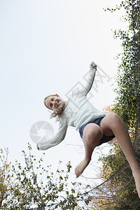 在花园蹦床上半空中跳跃的女孩图片