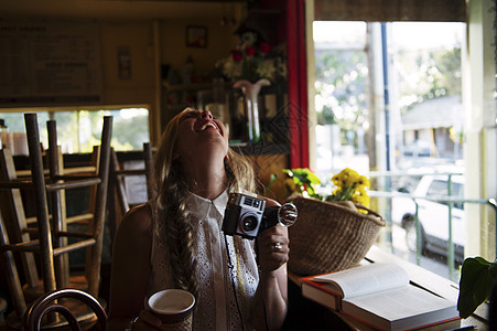 在咖啡馆拿着相机仰头大笑的年轻女子图片