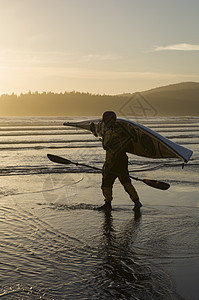 男子在沙滩上扛着皮划艇图片