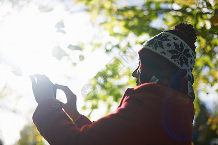 秋季公园里使用手机拍照的年轻女性图片