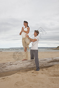 私人教练在海滩上帮助怀孕妇女做瑜伽动作图片