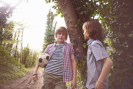 男孩夹着足球靠在树上说话图片