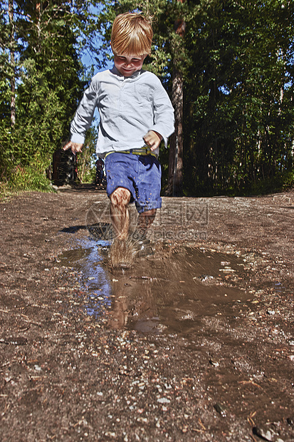 年轻男孩在泥水坑里跑过图片