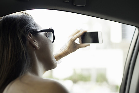 年轻女子在出租车窗口用智能手机拍照图片