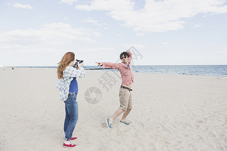 情侣在海滩用即时照相机拍摄图片