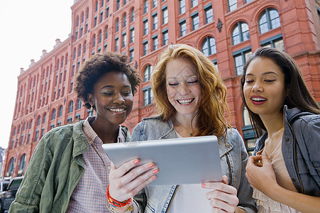 三名年轻妇女在街上看平板图片
