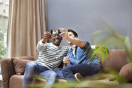 两个年轻人在客厅沙发上使用手机自拍图片